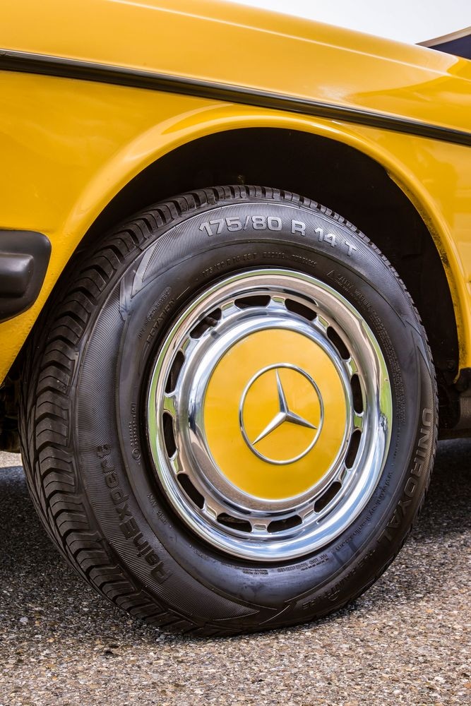 Mercedes-Benz 230 konštrukčného radu 123. Detailný pohľad na ľavé predné koleso s klasickou puklicou.